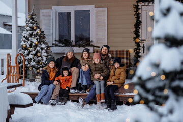 A large family in winter clothes and sweaters poses on the porch of a private country house on...