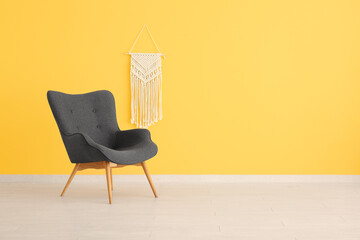 Stylish black armchair and wicker decor near yellow wall