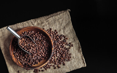 Coffee beans composition with a scoop and burlap bag on dark background, top view. Heap of roasted Arabica grains in a wooden bowl, decor or design element for coffee shop in rustic style.