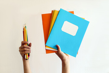 Back to school: children's hands hold notebooks and colored pencils on a light background