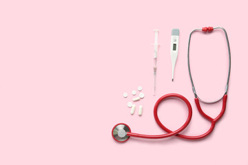 Medical stethoscope, pills, syringe and digital thermometer on pink background