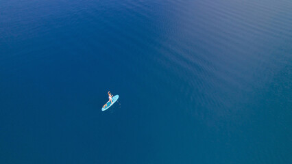 Fototapeta na wymiar AERIAL: Intense deep blue sea water and pretty lady paddling on SUP with her dog