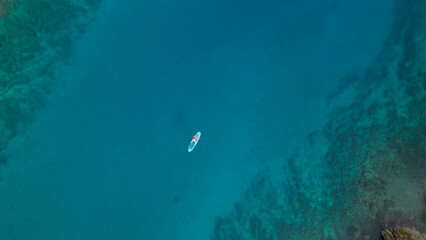 AERIAL TOP DOWN: Young lady stand up paddling in stunning clear blue sea water
