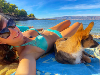 SELFIE: Happy young lady enjoys sunbathing on pebble beach with her cute puppy