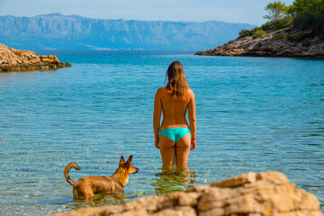 Back view of a beautiful woman with a dog standing in sea before going for swim