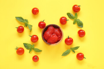 Composition with basil, canned and fresh tomatoes on yellow background