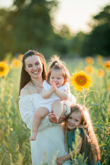 Beautiful young dark haired mother plays with her daughters in field of sunflowers in the sun. Family. Summer.