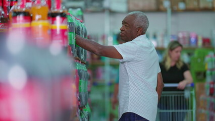 African American older shopper at supermarket searching for product to buy at soda shelf aisle