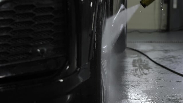 Close up. The alloy wheel of a black executive car of an expensive class is washed with a high-pressure washer at a car wash.