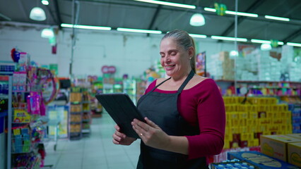 Female employee using tablet device standing inside supermarket. Woman staff using modern technology device checking inventory