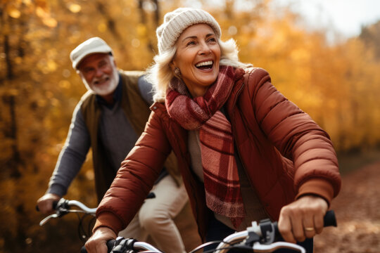 Happy active senior couple riding bicycles in autumnal park with yellow leaves.