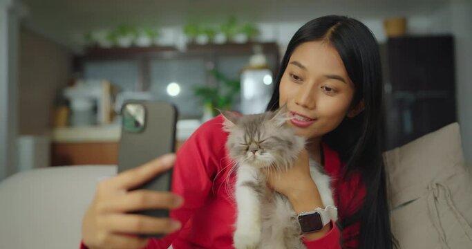 Young beautiful asian woman selfie with cat in living at home. She using phone to talking photo or record video with her pet at home.