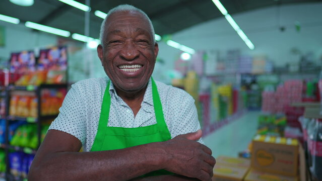 One Joyful Black Senior Staff Of Supermarket Smiling At Camera Standing Inside Grocery Store Aisle With Friendly Charismatic Expression