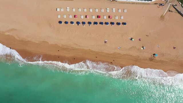 Straight down aerial footage of the beautiful beach front of Albufeira in Portugal, showing the Praia do Inatel Beach and the waves crashing on the golden sandy beaches on a sunny summers day.