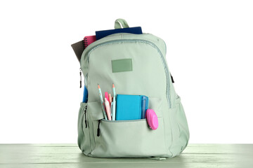Green school backpack with notebooks, pencils and pens on wooden table near white background