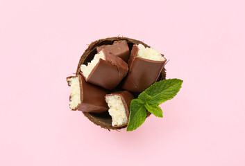 Coconut shell with tasty chocolate covered candies on pink background