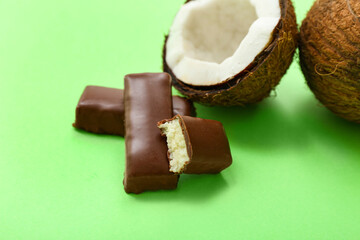 Tasty chocolate covered coconut candies on green background