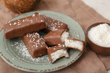 Plate with tasty chocolate covered coconut candies on table