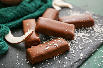 Board with tasty chocolate covered coconut candies on green background