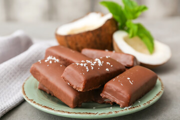 Plate with tasty chocolate covered coconut candies on grey background
