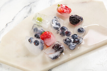 Board with frozen berries in ice cubes on white background