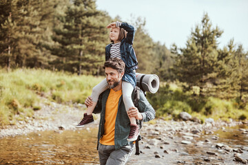 Father carrying his daughter while crossing a creek while they are hiking in the forest