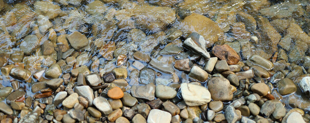 Shallow stream with rocks and pebbles. The rocks are various sizes and colors, including brown,...