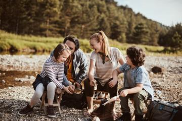 Young family camping by a creek and cooking fish by the campfire