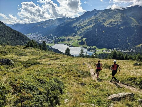 Trail running group runs down above Davos Klosters in the direction of Lake Davos. Running in the mountains. Beautiful trailrun landscape in Switzerland. High quality photo