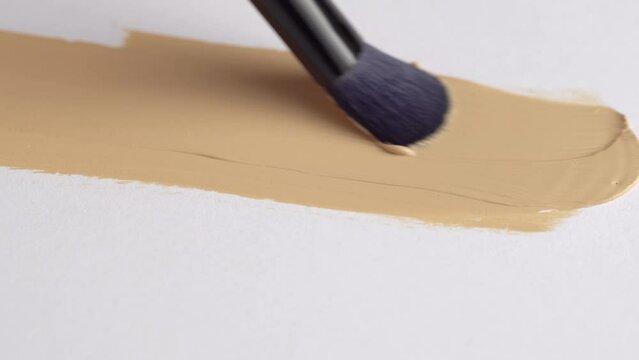 A smear of foundation cream or concealer with a brush on a white background, macro. Texture of cosmetic liquid foundation or beige cream smudge, smear, stroke. Advertising of professional cosmetics.