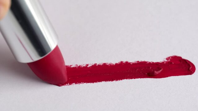 A woman's hand with red lipstick making a mark on a white background. Cosmetic lip gloss, lipstick smudge, smear. Smears of lip gloss applicator on a white background.