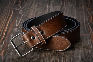 Rolled men's leather belt with metal buckle on wooden desktop