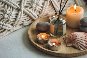 Obraz na płótnie Canvas Apartment natural aroma diffusor with sea breeze fragrance. Burning candles on bamboo tray, cozy home atmosphere. Relaxation, detention zone in the living or bedroom. Stones as decor