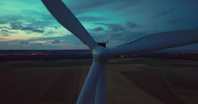 Aerial view wind turbines generate renewable energy at night. Silhouettes of windmills with bright lights on propellers rotate against dark sky