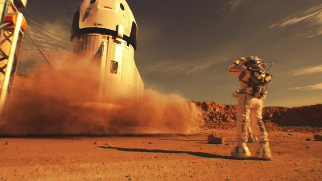 Two astronauts in spacesuits stand, watch spacecraft landing on Mars surface. Manned space mission on red planet. Technological advance of the future. Futuristic colonization and exploration concept.