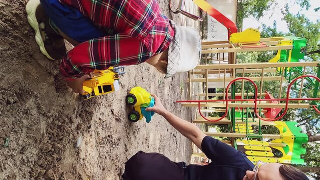 Vertical video - father and son play with car models in the sandbox in summer. Concepts role-playing game, family walk, parental attention, upbringing, development, recreation, unity, happy childhood