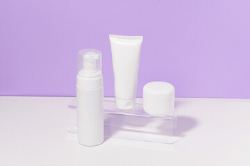 Fototapeta na wymiar Horizontal image of a white mockup set of a tube and a jar of cream and foam on a purple background. The concept of daily care cosmetics for the face and body, moisturizing and beauty treatments