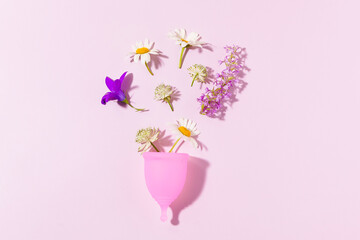 Pink reusable menstrual cup with flowers on pink isolated background. Hygiene products, female menstrual cycle and ecological alternative concept.