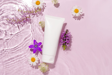 Fototapeta na wymiar White mockup of a tube of cream or lotion on a pink background with water waves and flowers. Salon facial care, beauty, spa, moisturizing and rejuvenation concept.