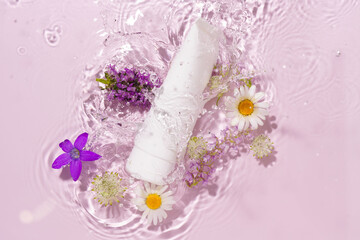 White mockup tube of cream falling into water with splashes and flowers on pink isolated...