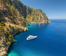 Aerial view of beautiful yacht on the sea in summer day. Butterfly Valley, Oludeniz, Turkey. Top drone view of bay, luxury boat, clear blue water, mountains and green trees. Travel. Rocky sea coast