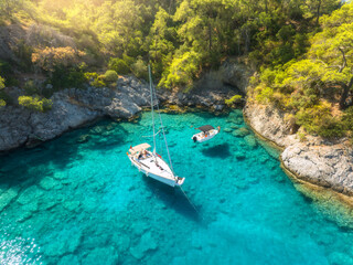 Fototapeta na wymiar Aerial view of beautiful yacht and sailboat on the sea at sunrise in summer. Oludeniz lagoons, Turkey. Top view of bay, luxury yacht, motorboat, clear blue water, beach, rocks and green trees. Travel