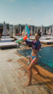 Bright girls in bikinis playfully splash water at each other with water guns.