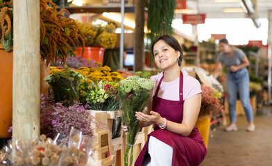 Smiling polite young asian female florist in apron working at flower market, offering bouquet of blooming ammi
