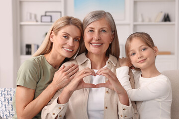 Three generations. Happy grandmother showing heart gesture with her daughter and granddaughter at home