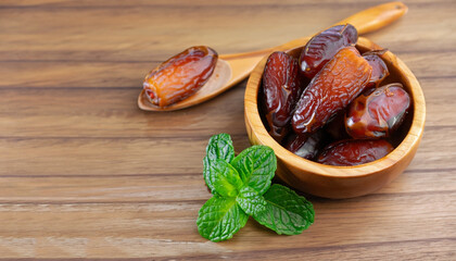 Date palm fruits in wooden bowl and spoon with mint green leaf isolated on wood table background.