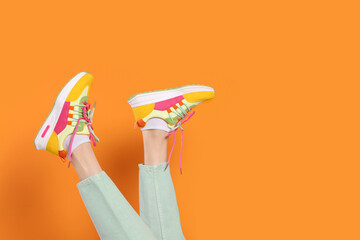 Woman wearing pair of new stylish sneakers on orange background, closeup. Space for text