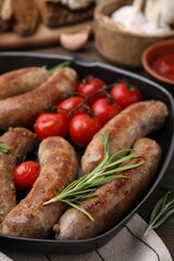 Grill pan with tasty homemade sausages, rosemary and tomatoes on table, closeup