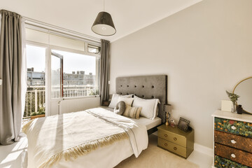 a bedroom with a bed, dresser and window overlooking the cityscapet is on the other side of the room