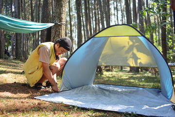Happy male tourist or traveler putting on a tent at camping site in the forest. A man outdoors in the process of setting up a tent.